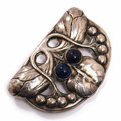 Evald Nielsen Skønvirkebroche af sølv rigt prydet med stiliseret bladornamentik og cabochonslebet lapis lazuli. L. ca. 7 cm. Ca. 1910-20.