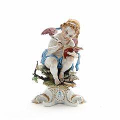 Figur af porcelæn i form af putto med pen og bog dekoreret i guld og farver, Cappo di Montes mærke. Ca. 1900. H. 23 cm.