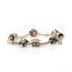 Pandora Armbånd af sterlingsølv med talrige charms prydet med facetslebne klare sten og kulturperle. L. ca. 19 cm. Ca. 2010.