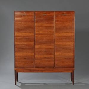 Dansk møbeldesign Skab af palisander opsat på løst stel med tilspidsende ben. Front med tre jalousilåger, bag hvilke interieur med små hylder.